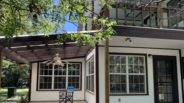 A covered patio area with a ceiling fan, a chair, and large windows. - Two story home with Las Moras Creek views (Brackettville)