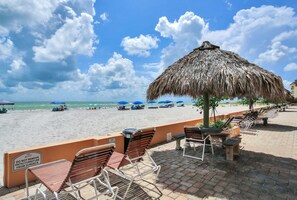 Un patio frente a la playa con sillas de metal y un toldo de paja, con vista al océano.