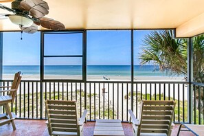 Un balcón con vista a la playa, dos sillas de madera y un ventilador de techo.