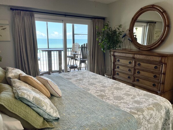 Un dormitorio con una cama grande, un aparador de madera, un espejo y vista al océano desde la ventana.