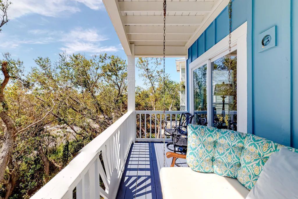 A covered porch with a white railing, a blue wall, and a patterned cushion.