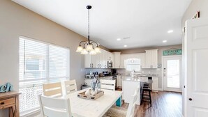 Una cocina moderna con armarios blancos, una isla central y un comedor con sillas blancas.