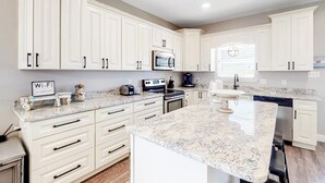 Una cocina moderna con armarios blancos, encimera de granito y microondas integrado.