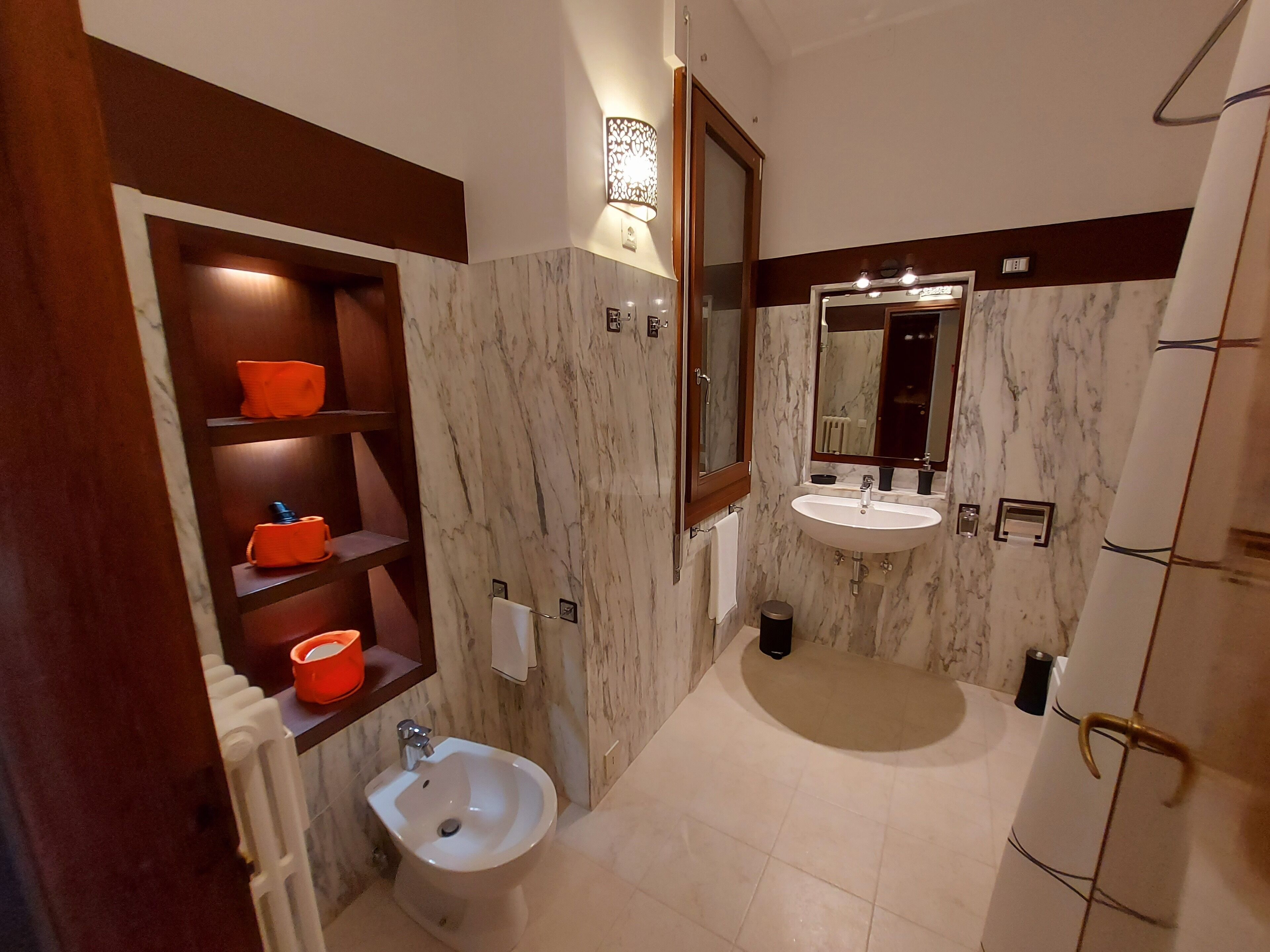 A bathroom with a marble vanity, a sink, a bidet, and a shelf with orange containers.