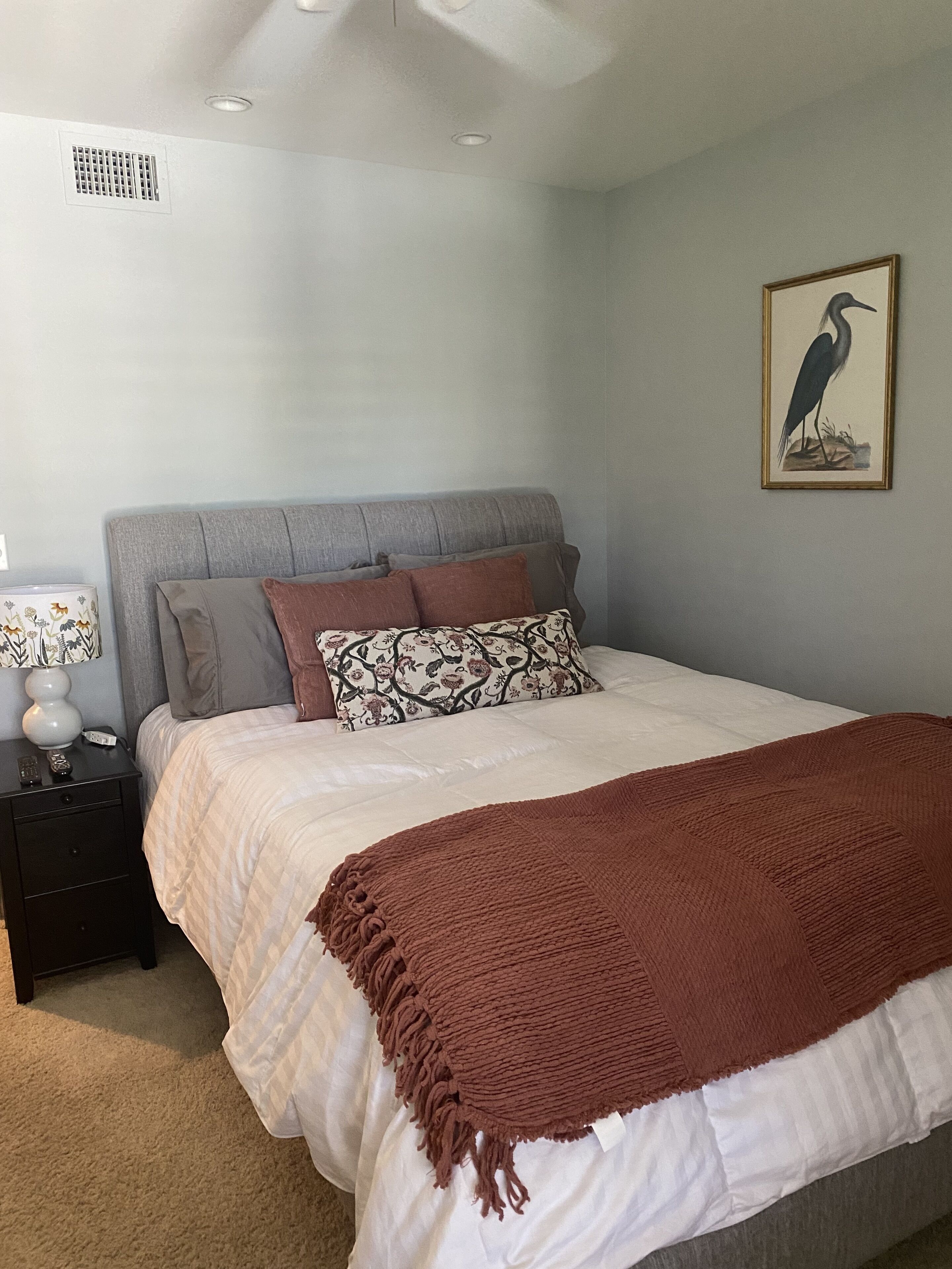 A bedroom with a bed, nightstand, lamp, and a framed picture on the wall.