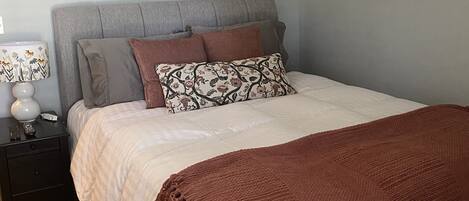 A bedroom with a bed, nightstand, lamp, and a framed picture on the wall.