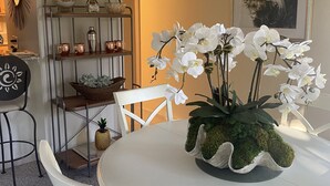 A dining area with a round table, white chairs, a white chandelier, and a potted orchid plant.