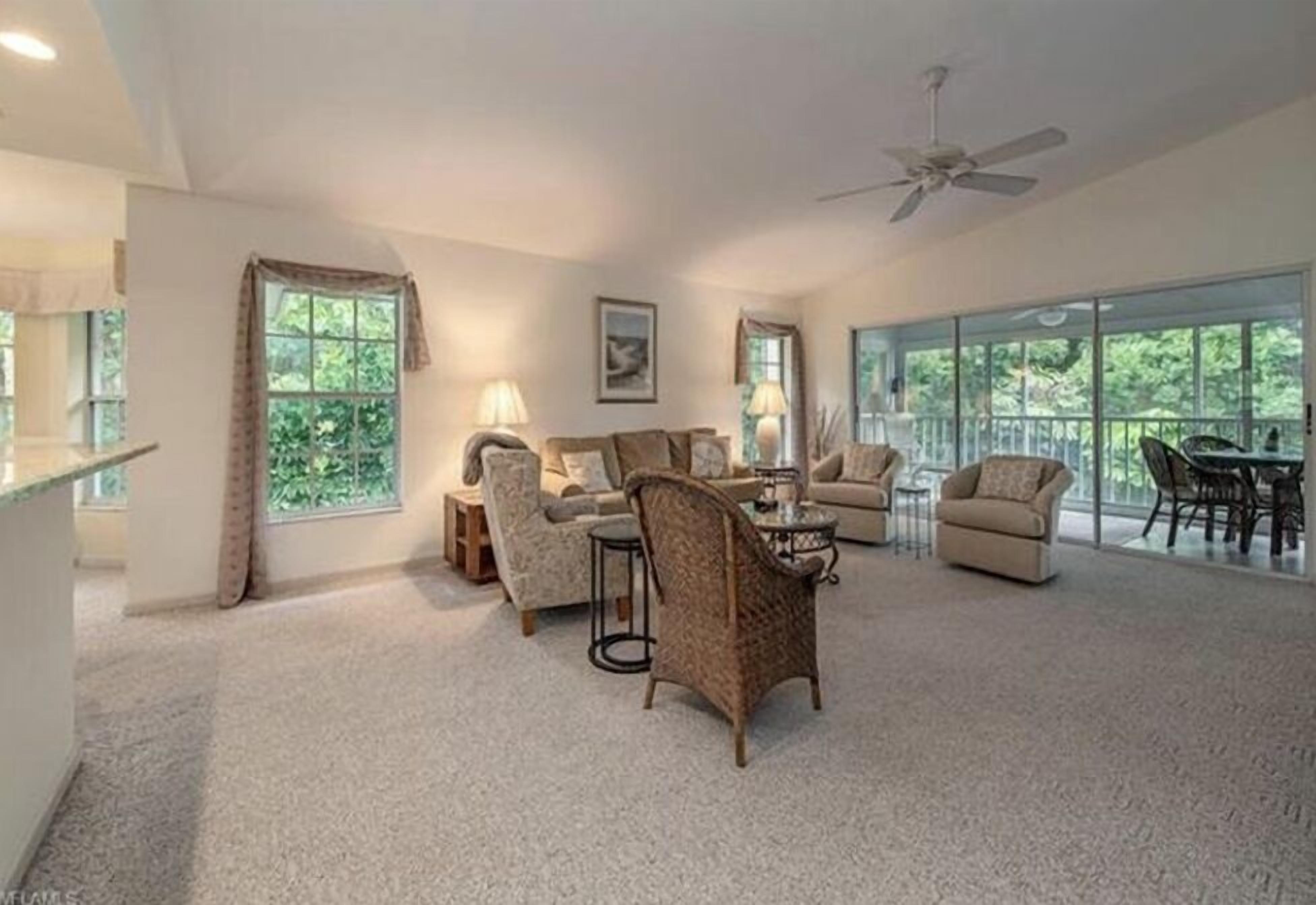 A spacious living room with a high ceiling, large windows, and a ceiling fan.