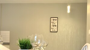 Ein Essbereich mit einem dunklen Holztisch, weißen Stühlen, einer Kühlpflanze und einem gerahmten Motivationsspruch an der Wand.