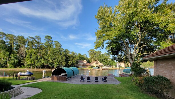 A lakeside deck with a covered seating area, a boat dock, and a swimming pool in the background.