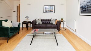 A modern living room with a leather sofa, a glass coffee table, and a green armchair. - The Bayswater Nook - Stylish 1bdr Flat (London)