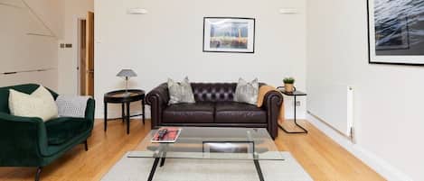 A modern living room with a leather sofa, a glass coffee table, and a green armchair.