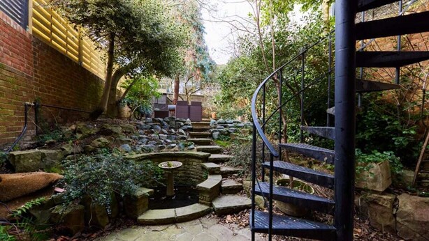 A stone pathway leading to a spiral staircase surrounded by greenery and a small pond. - The Bayswater Nook - Stylish 1bdr Flat (London)