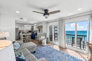 Relax in a spacious living area with ocean views through expansive glass doors, featuring a sofa, dining area, and fully equipped kitchen.