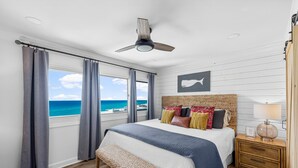 Een slaapkamer met een bed, een plafondventilator, een nachtkastje met een lamp en uitzicht op de oceaan.