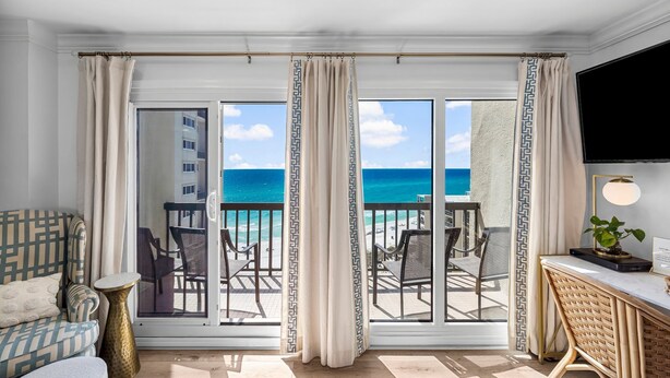Een kamer met balkon en uitzicht op het strand, met een bank, een klein tafeltje en een televisie.