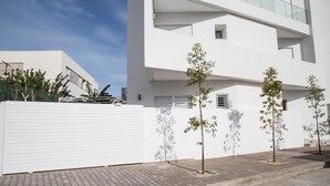 Ein modernes Gebäude mit weißer Fassade, mehreren Balkonen und einem gepflasterten Weg mit jungen Bäumen.