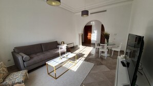 Ein modernes Wohnzimmer mit grauem Sofa, einem Couchtisch, einem Fernseher und einem Essbereich mit Stühlen und einem Glastisch.