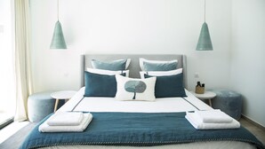 A neatly arranged hotel room with a bed, two bedside tables, a small round table, and a blue ottoman. - Villa Bonheur Villa Exceptionnelle la Soukra (La Soukra)