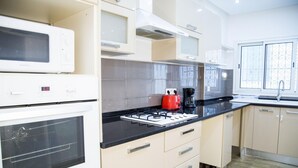 A modern kitchen with white cabinetry, a black countertop, a red kettle, and a coffee maker. - Apt Moderne Face au Parc et au c ur de la Marsa (La Marsa)