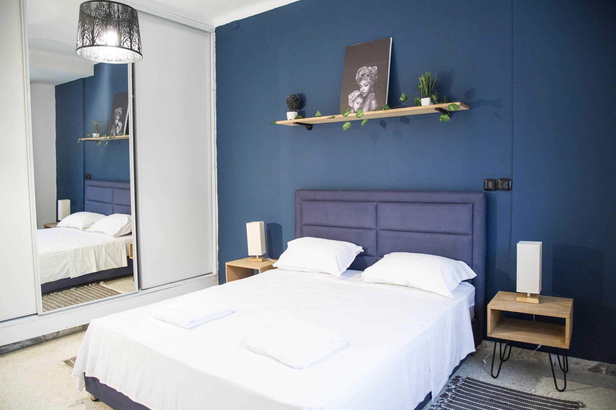 Une chambre à coucher moderne avec un grand lit, deux tables de chevet, un miroir et une étagère murale agrémentée d’objets décoratifs.