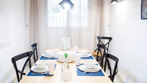 A dining area with a wooden table set for four, black chairs, a hanging light fixture, and a window with decorative iron bars. - Apt Moderne Face au Parc et au c ur de la Marsa (La Marsa)