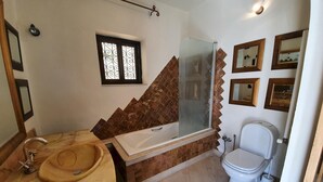 Et badeværelse med badekar, vask, toilet og bruser.