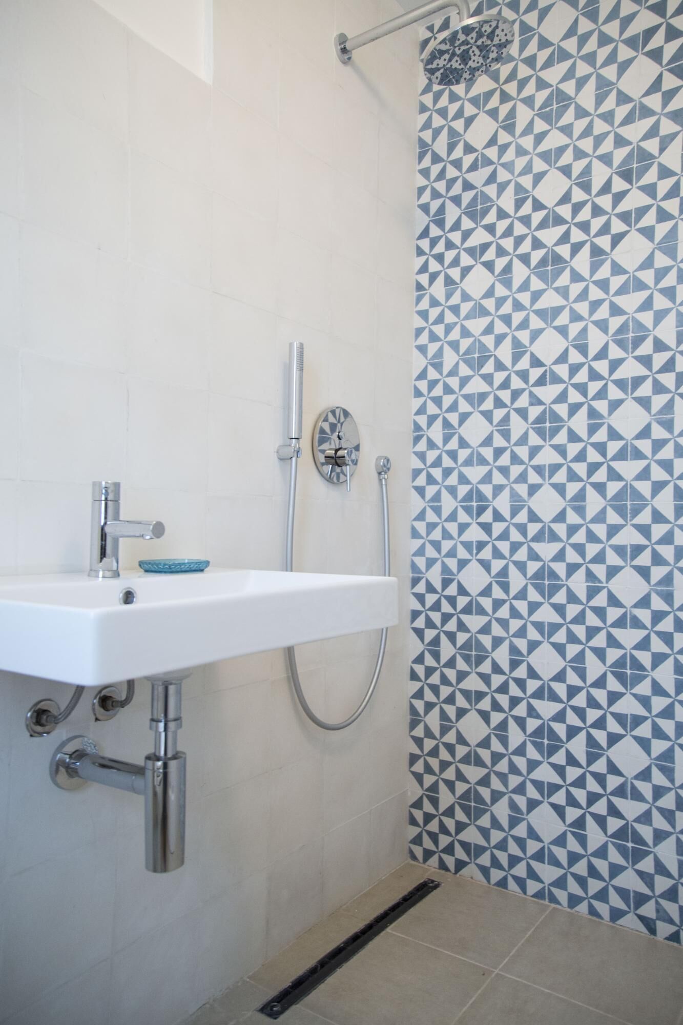A bathroom with a white sink, a handheld showerhead, and a wall with a geometric tile pattern.