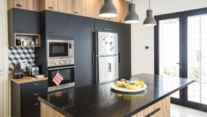 A modern kitchen with a black countertop, stainless steel appliances, and pendant lighting. - Les Verrières De Gammarth: Villa moderne +Piscine (La Marsa)