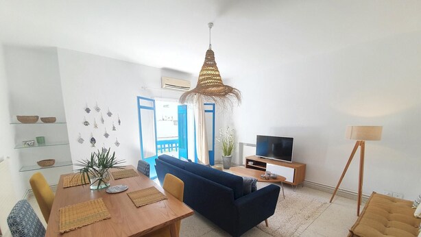 Una sala de estar moderna con una mesa de comedor de madera, un sofá azul y un televisor sobre un mueble de madera.