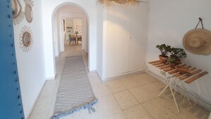 Un pasillo con alfombra estampada, lámpara colgante, espejos en la pared y plantas en macetas.