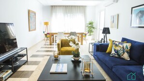 Ein modernes Wohnzimmer mit Sofa, Couchtisch, Fernseher und einem Essbereich mit Stühlen und Tisch.