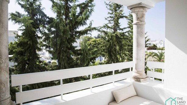 Ein Balkon mit einer weißen Bank, einer Steinsäule und Bäumen im Hintergrund.