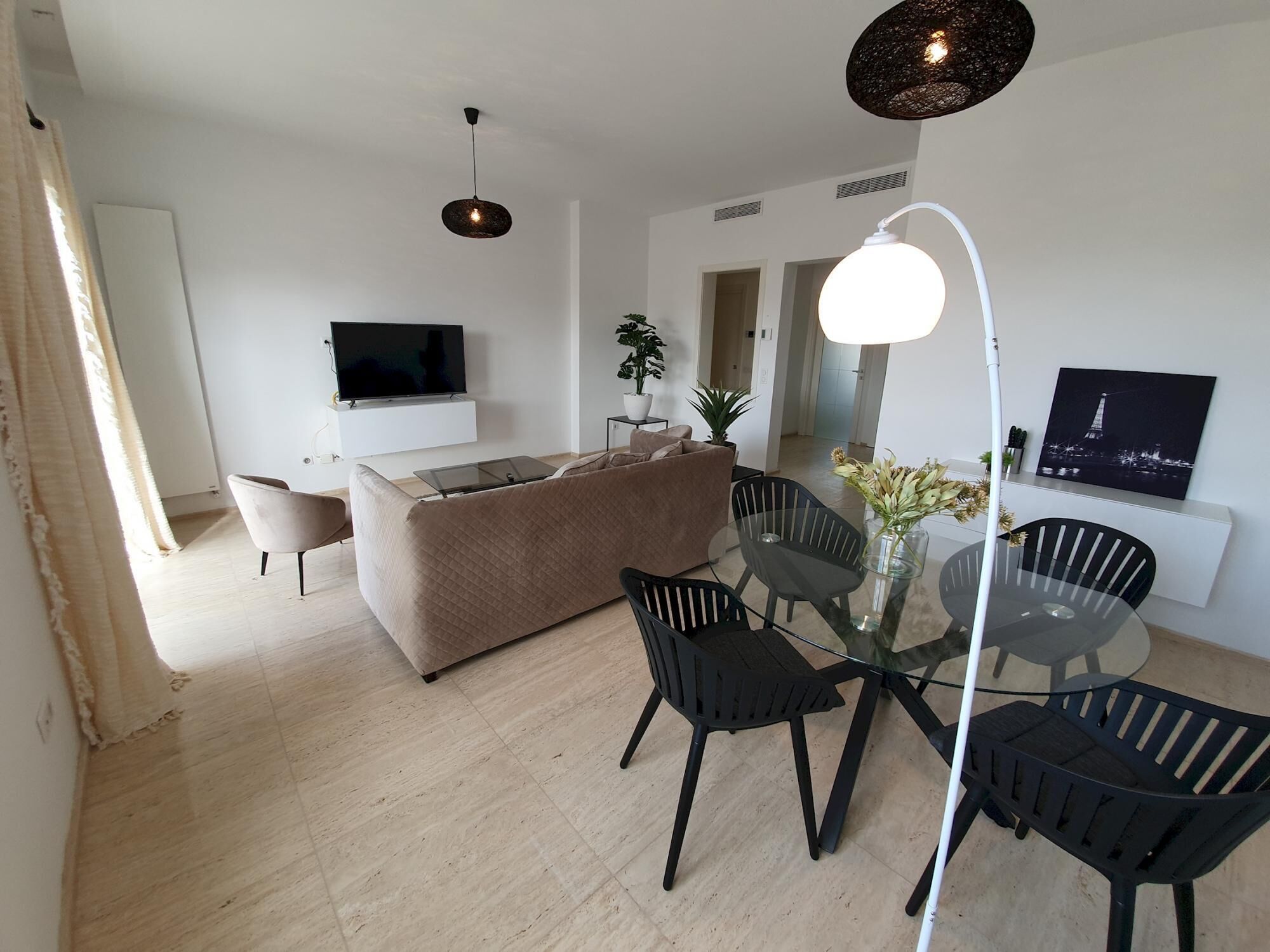 A modern living room with a sofa, TV, and dining area with chairs and a table.
