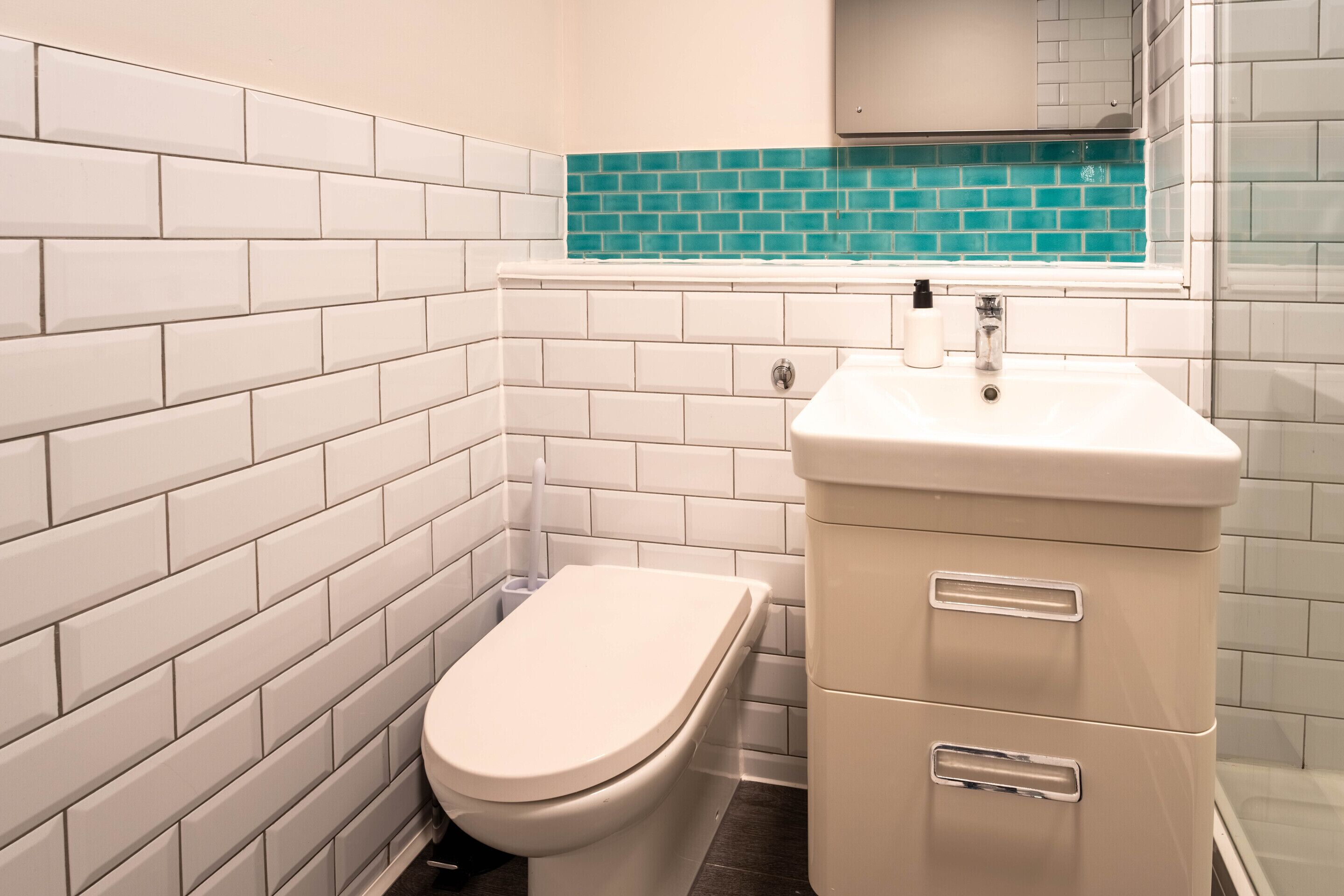 Un bany amb parets de rajola blanca, un vàter blanc i un lavabo amb un mirall a sobre.