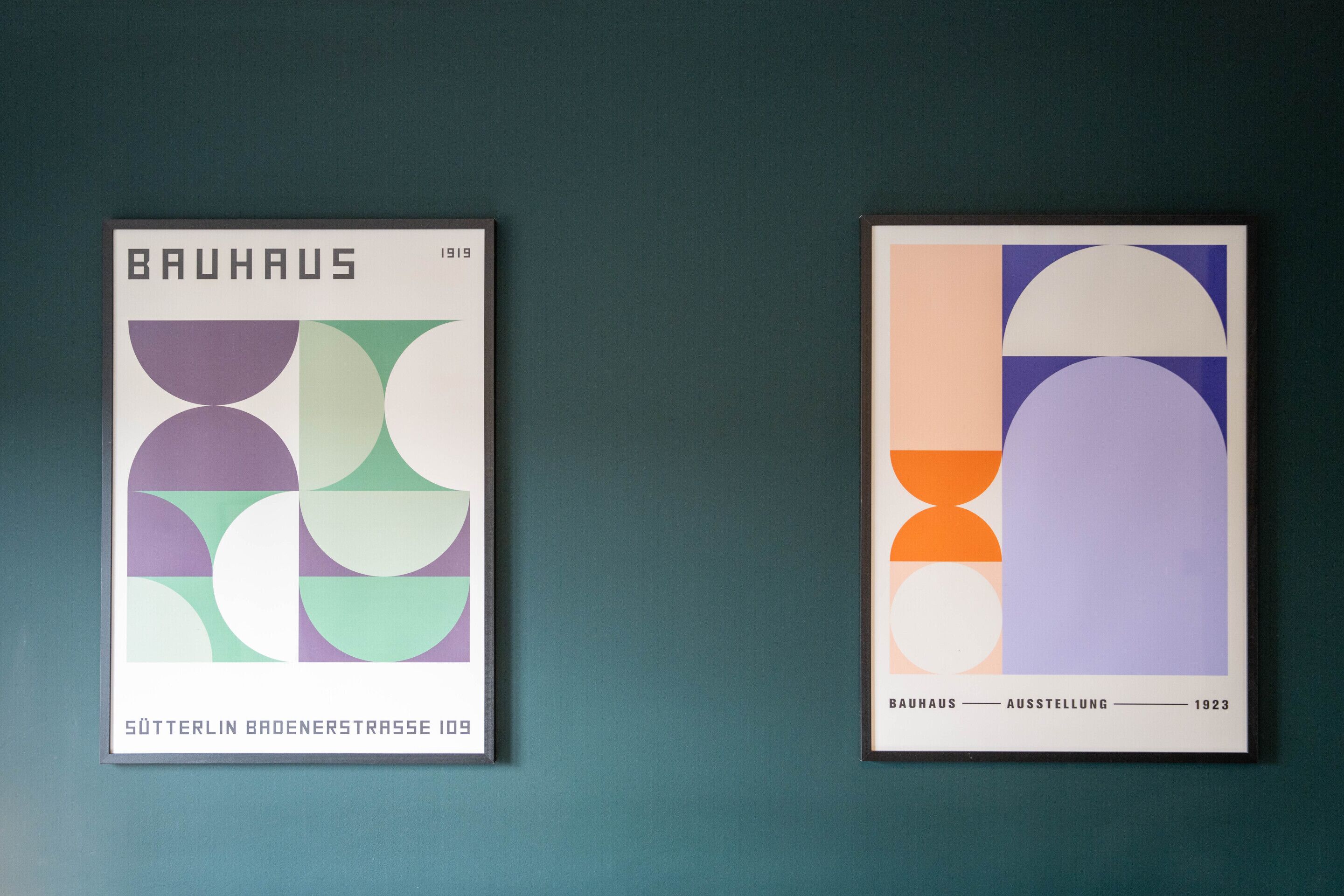 Twee ingelijste kunstwerken met geometrische vormen en tekst, bevestigd aan een muur in blauwgroen.