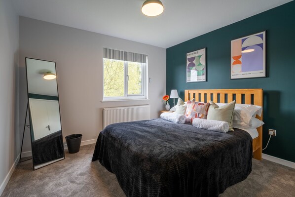 A bedroom with a bed, a large mirror, a window, and artwork on the wall.
