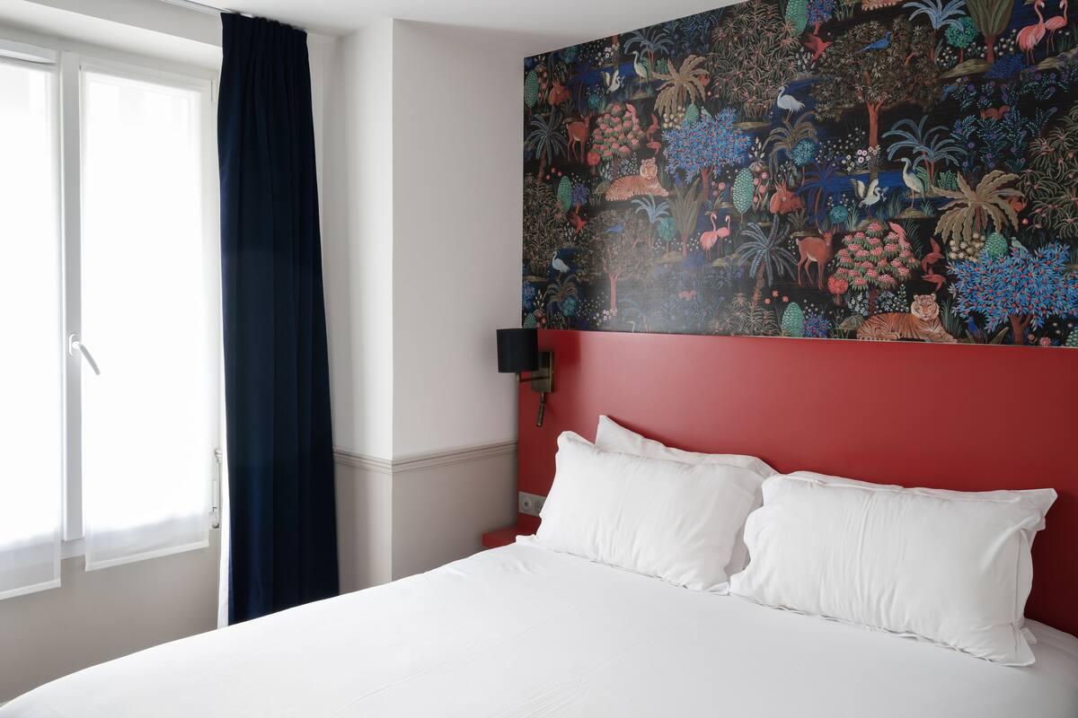 A hotel room with a large bed, a red accent wall, and a colorful mural.