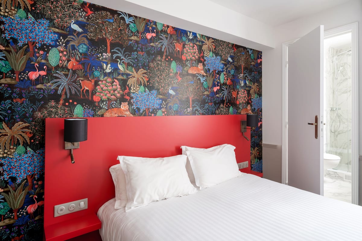 A bedroom with a red headboard, white bedding, and a vibrant mural on the wall.