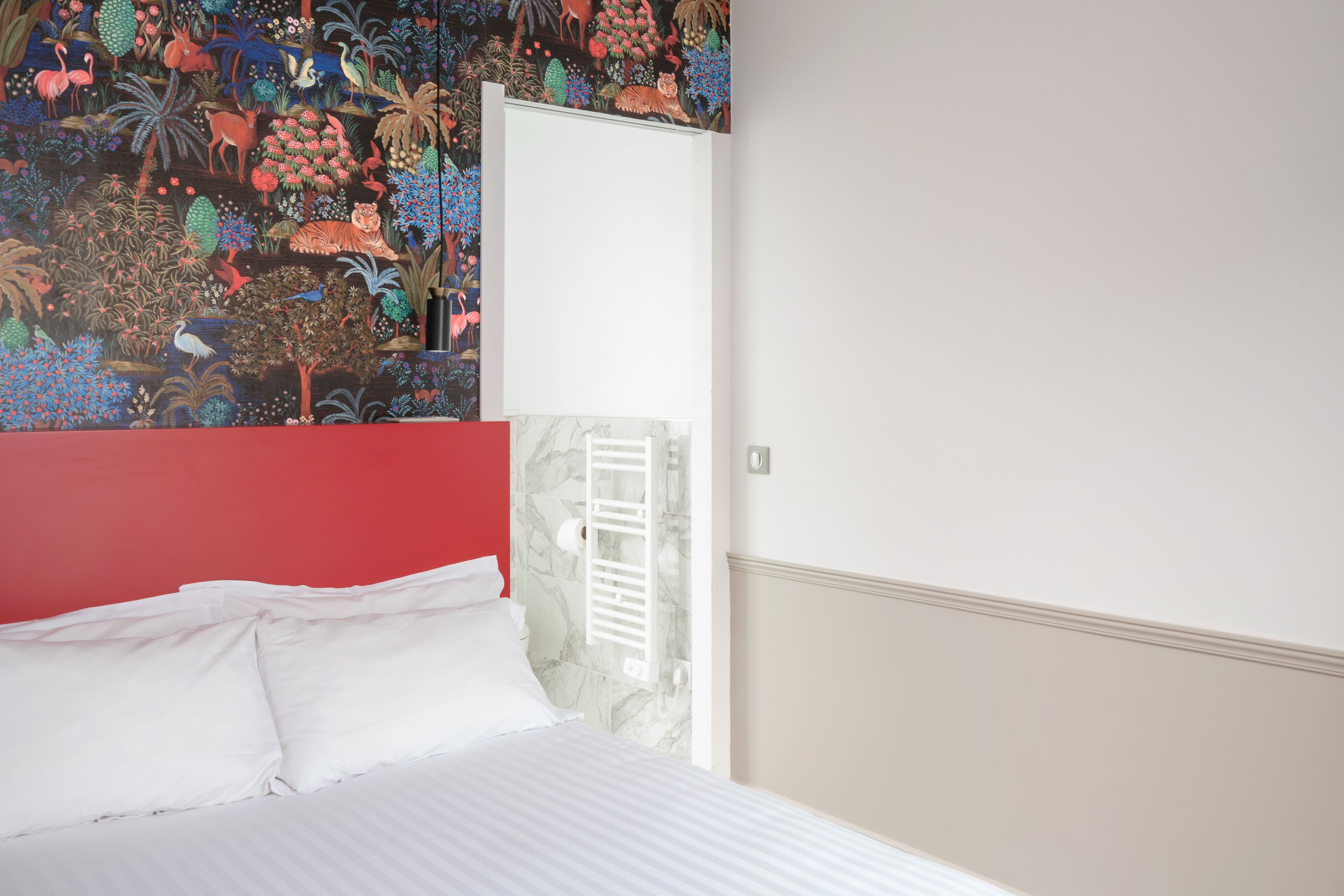 A hotel room with a bed, a red headboard, a mural with tropical wildlife, and a white door.