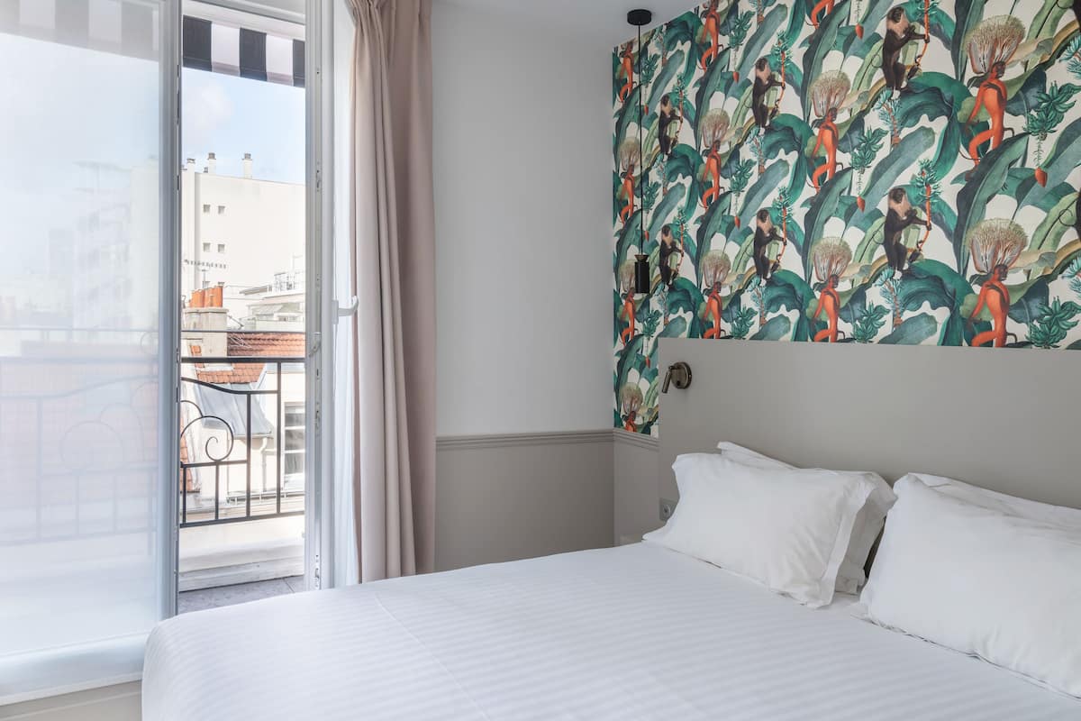A hotel room with a bed, a window with curtains, and a wall with a patterned mural.