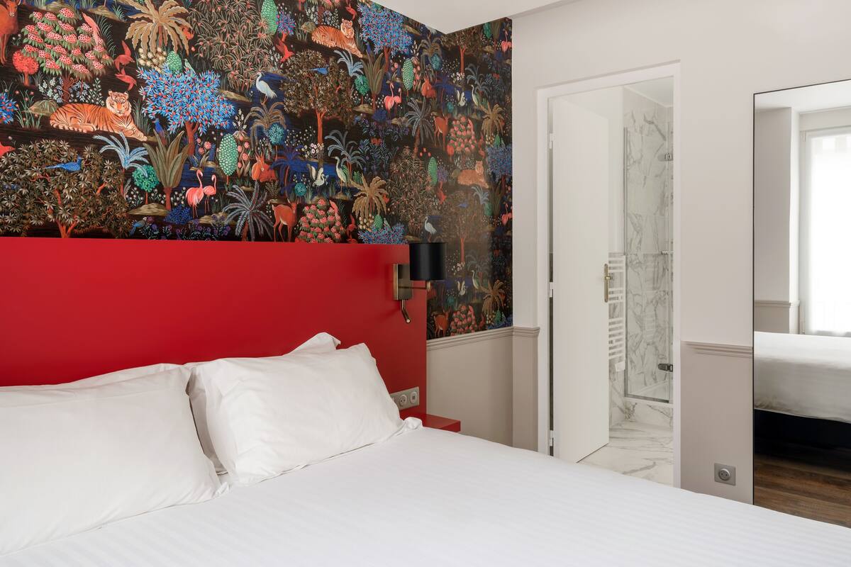 A bedroom with a red headboard, white bedding, and a colorful mural on the wall.