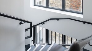 Una escalera moderna con barandillas negras y vista a una pared de ladrillo a través de amplios ventanales.