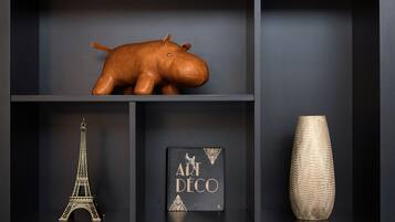 Ein Regal mit einem braunen Leder-Flusspferd, einem goldenen Modell des Eiffelturms, einem Buch mit dem Titel 'ART DECO' und einer strukturierten Vase.