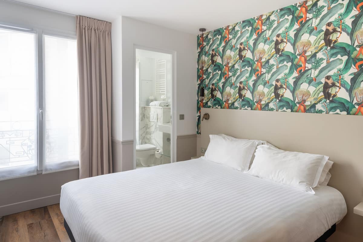 A hotel room with a large bed, a bathroom with a glass shower enclosure, and a view of the outside balcony.