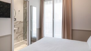 Habitación de hotel con cama, zona de ducha con baldosas de mármol y un ventanal con cortinas.