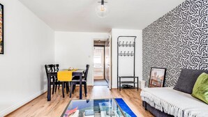 A modern living room with a glass coffee table, a sofa, a patterned wall, and a dining area with chairs and a table. - The St Clements Townhouse 3 Bedroom Bijou Central (Oxford)