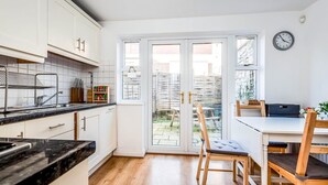 A modern kitchen with white cabinets, a black countertop, and a dining area with wooden chairs and a table. - The St Clements Townhouse 3 Bedroom Bijou Central (Oxford)