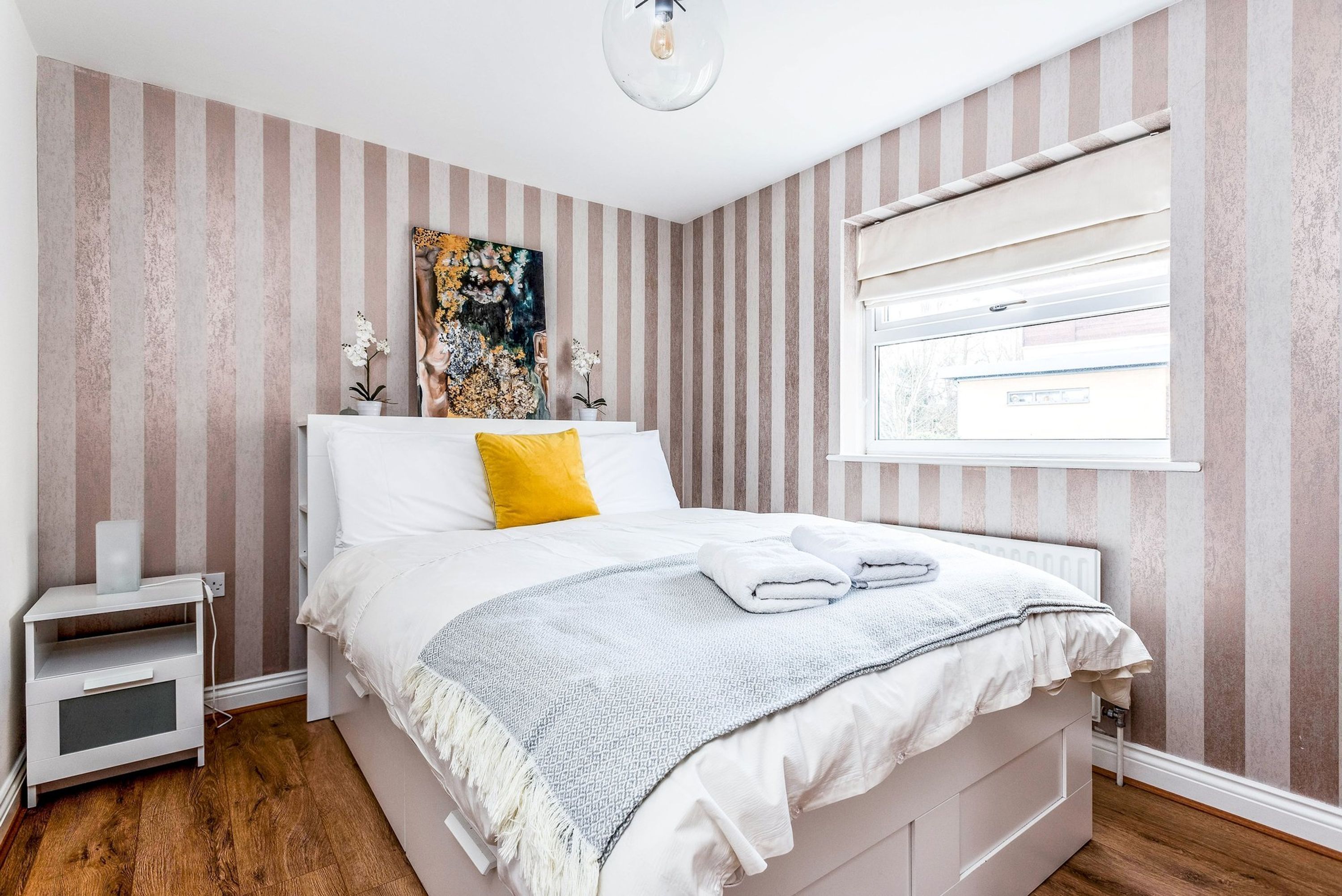 A bedroom with a bed, bedside table, and a window with blinds.