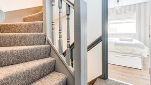 A staircase with a textured carpet and wooden balusters leading to a bedroom with a bed and a nightstand. - The St Clements Townhouse 3 Bedroom Bijou Central (Oxford)